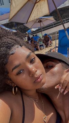 two women are sitting under an umbrella on the beach, one has her arm around the other's shoulder