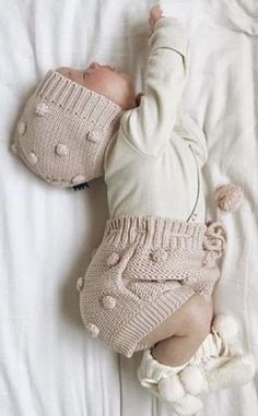 a baby laying on top of a bed wearing a knitted outfit