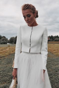 a woman wearing a white dress and holding a straw in her hand while standing on a field