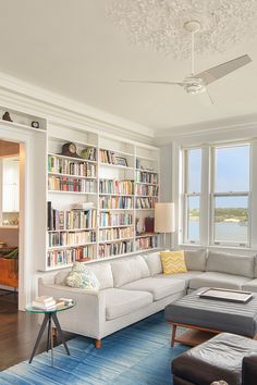 a living room filled with furniture next to a window covered in lots of book shelves