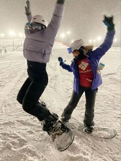 two people on snowboards in the snow at night