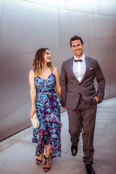 a man in a suit and tie walking next to a woman wearing a floral dress