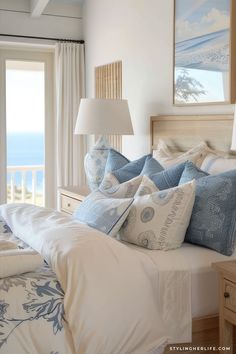 a bed with blue and white pillows in a bedroom next to a window overlooking the ocean