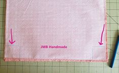 a piece of pink fabric with the words jmb handmade on it next to a blue pen