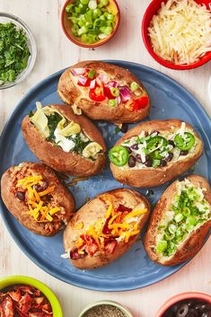 several baked potatoes on a blue plate surrounded by bowls of salads and condiments