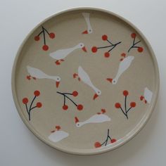 a white plate with red berries and birds painted on the side, sitting on a table