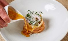 a person pouring sauce onto a dish on a white plate with parmesan cheese