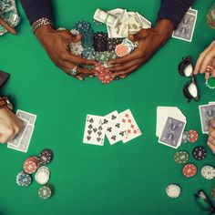 several people are holding their hands over playing cards and poker chips on a green table