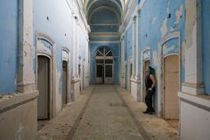 a woman is standing in an empty hallway with blue walls and peeling paint on the walls