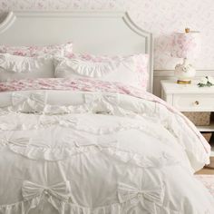 a white bed with pink and white comforter in a bedroom next to a night stand