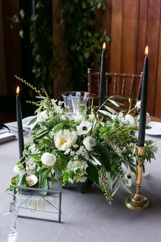 a table with candles and flowers on it in front of a mirror box filled with greenery