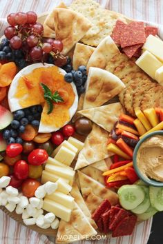 an assortment of cheeses, crackers and fruits on a platter with dip