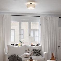 a living room filled with furniture and white curtains on the window sill, next to a coffee table