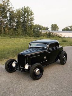 an old black car is parked on the side of the road