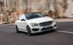 a white mercedes cla driving down a road next to a stone cliff side wall