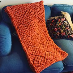 an orange knitted pillow sitting on top of a blue couch next to a cushion