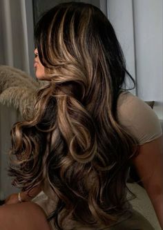 a woman with long, wavy hair sitting in front of a window looking out the window