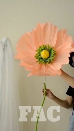 a woman holding a large pink flower in front of a white wall with the word fac on it