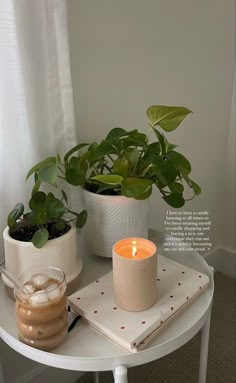 a white table topped with a potted plant next to a candle on top of a book