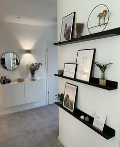 three black shelves with pictures and plants on them in front of a white wall that has a mirror above it