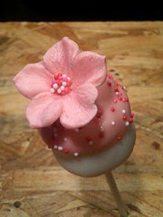 there is a pink flower on top of a white cake lollipop with sprinkles