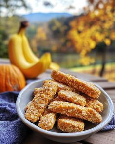 a white bowl filled with granola bars on top of a wooden table next to bananas