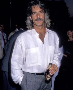 a man in a white shirt and grey pants holding a beer bottle with one hand