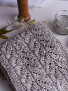 a close up of a knitted blanket on a table with flowers and candles in the background