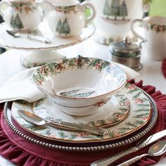 a white table topped with plates and cups filled with saucers covered in holly leaves