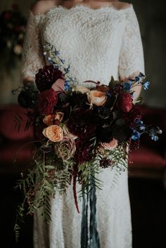 a woman holding a bouquet of flowers in her hands and wearing a white dress with lace sleeves