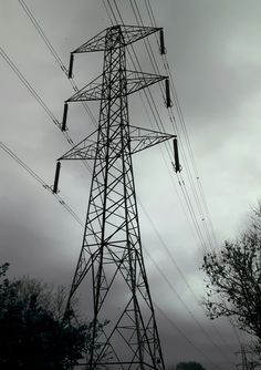 an electric tower with many wires above it and trees below in the foreground on a cloudy day