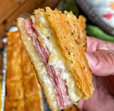 a person holding up a sandwich with meat and cheese on it in front of bread sticks