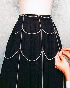 a woman is wearing a black skirt with white stitching