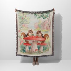 a woman holding up a tapestry with two chipmuns sitting on top of a mushroom