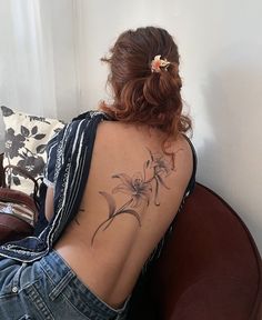 a woman sitting on a couch with her back turned to the camera and tattoos on her upper half