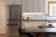 a stainless steel refrigerator in a kitchen with white cabinets and black countertops, along with a cutting board that has fruit on it