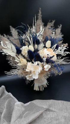 an arrangement of dried flowers and feathers on a table cloth with a gray linen background