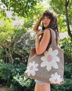 a woman carrying a brown crocheted bag with flowers on the front and sides