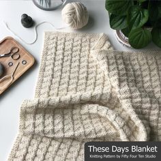 a knitted blanket sitting on top of a table next to yarn, scissors and a potted plant