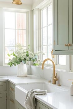 a white kitchen with gold faucet and green cabinetry on the windowsill