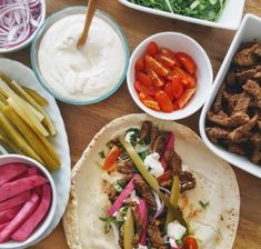 several different types of food in bowls on a wooden table with dips and pita bread