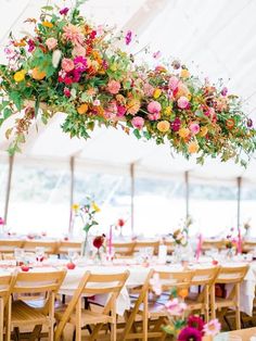 an outdoor tent with tables and chairs covered in floral arrangements hanging from the ceiling over them