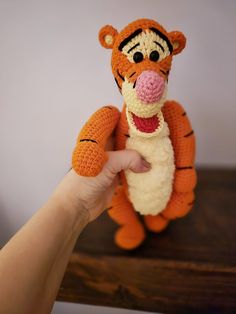 a crocheted stuffed animal is being held by a person's hand on a wooden table