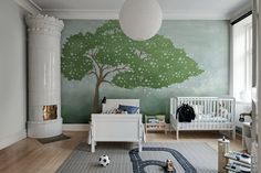 a baby's room with a green tree painted on the wall and white crib