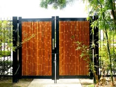 a wooden gate in front of a lush green tree filled yard with tall bamboo trees