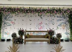 a bench sitting in front of a wall with flowers and greenery hanging from it