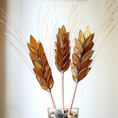 three dried plants in a glass vase filled with rocks