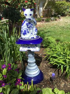 a blue and white cat statue sitting on top of a flower pot in the garden