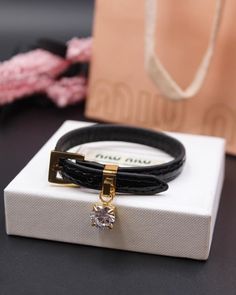 a black leather bracelet with a gold plated clasp and a crystal stone on it