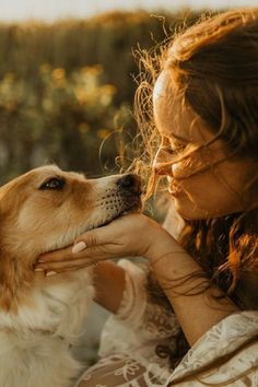 a woman is petting her dog outside in the sun with long brown hair and eyes closed